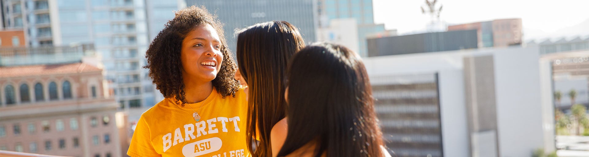 Three female Barrett students having a conversation on a balcony overlooking the Barrett Downtown campus