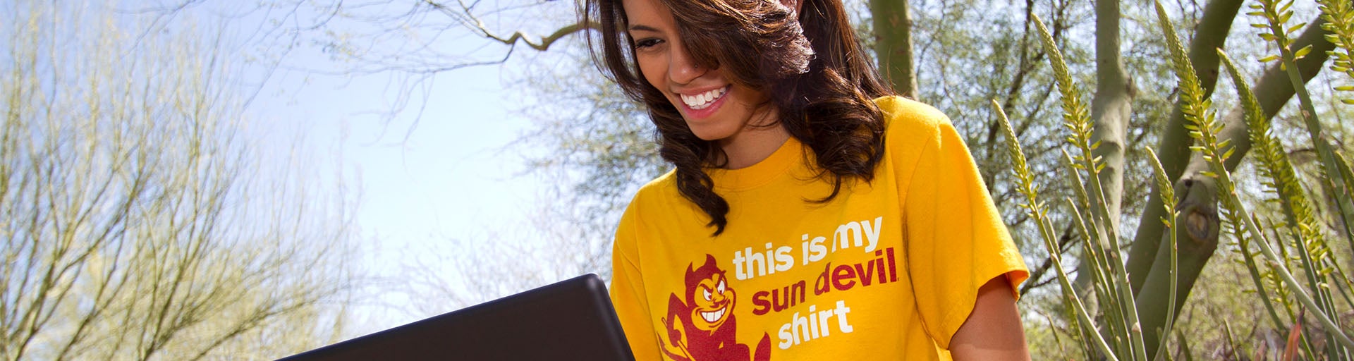 Female student wearing a gold ASU shirt on her laptop