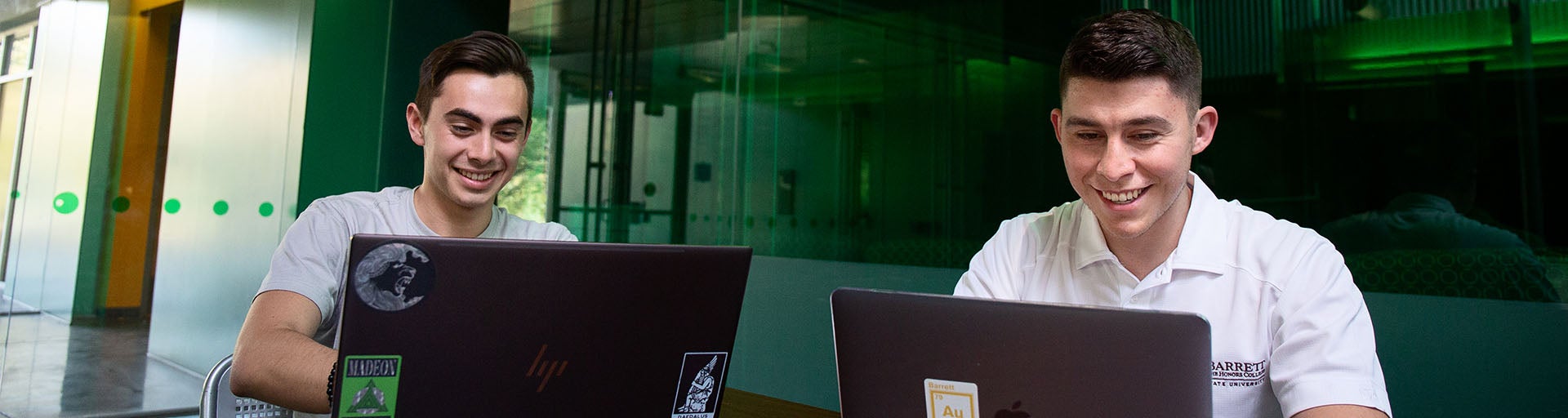 Two students engaging on their laptops and smiling