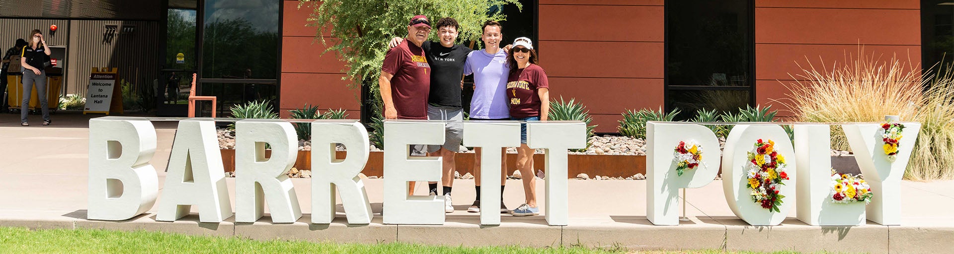 Barrett family posing outside of the Barrett Poly campus with the Barrett Poly sign in the front