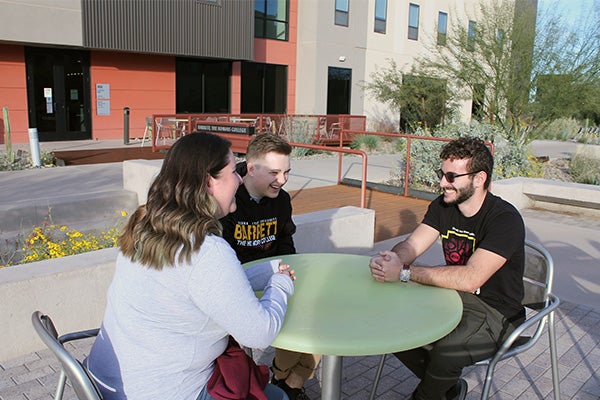 Several students sitting on a table outside Lantana Hall at the Poly campus
