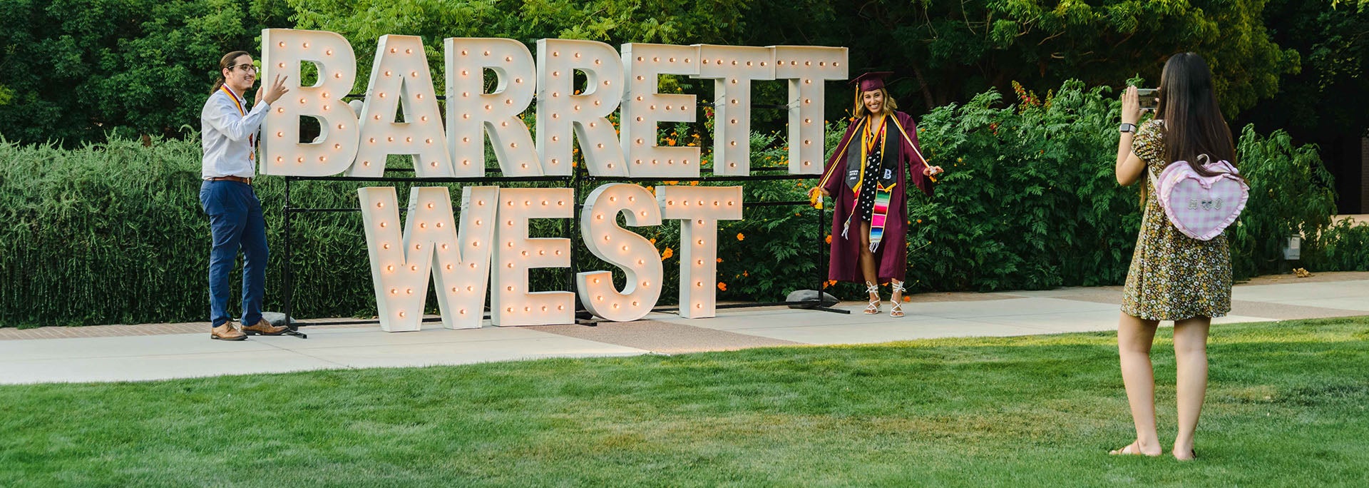 Two students posing in professional and graduation attire in front of Barrett West sign at the Barrett West campus