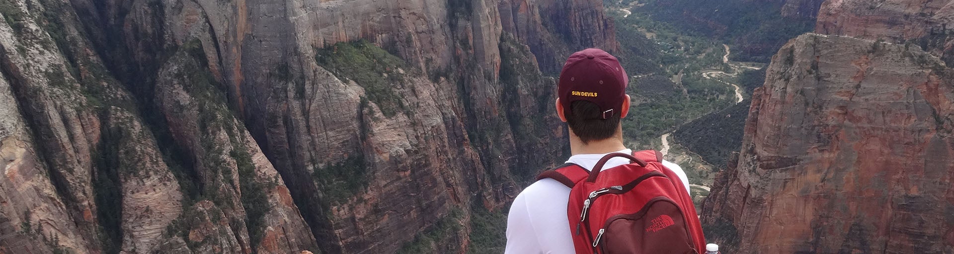 Student wearing a backpack and hat, overlooking an Arizona canyon