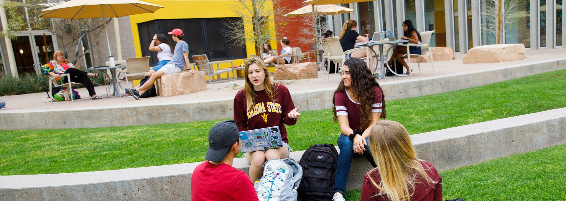 Four students gathered around the Barrett Tempe great court lawn having a conversation