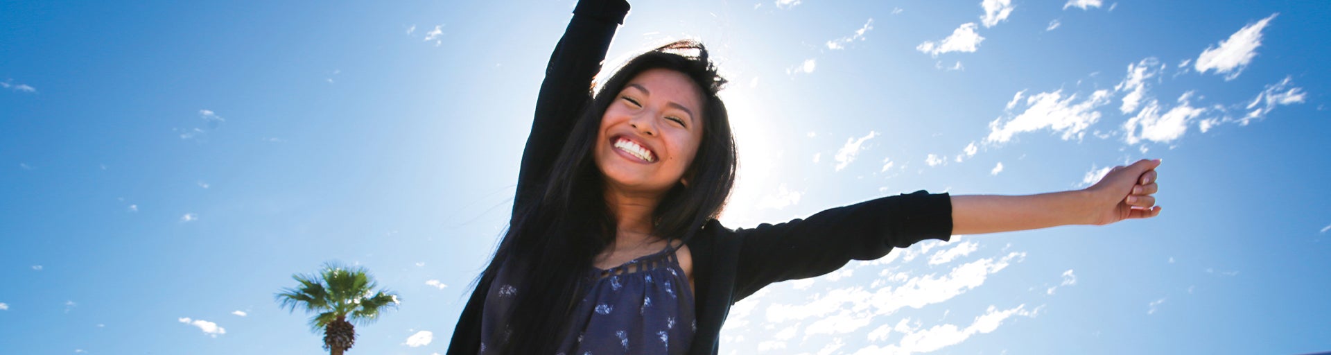 Female student smiling and reaching towards the sky