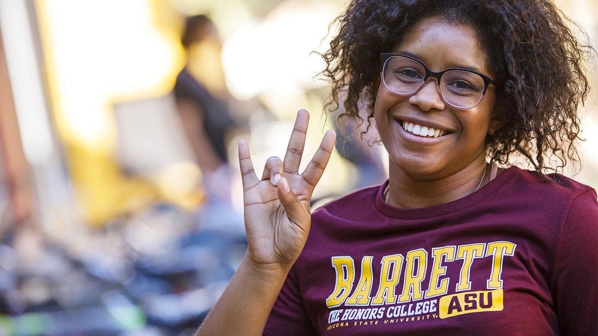 Female student with Barrett shirt smiling and posing with the ASU pitchfork sign
