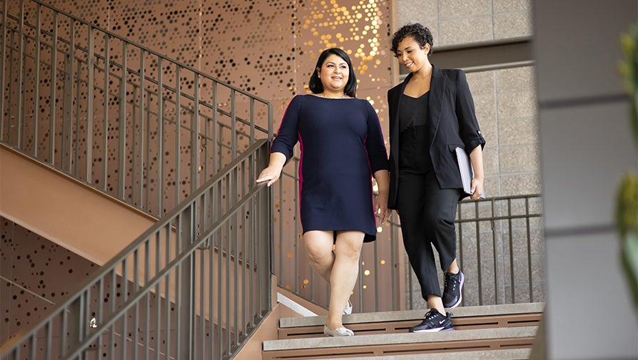 Two people in business attire having a conversation while walking down a flight of stairs