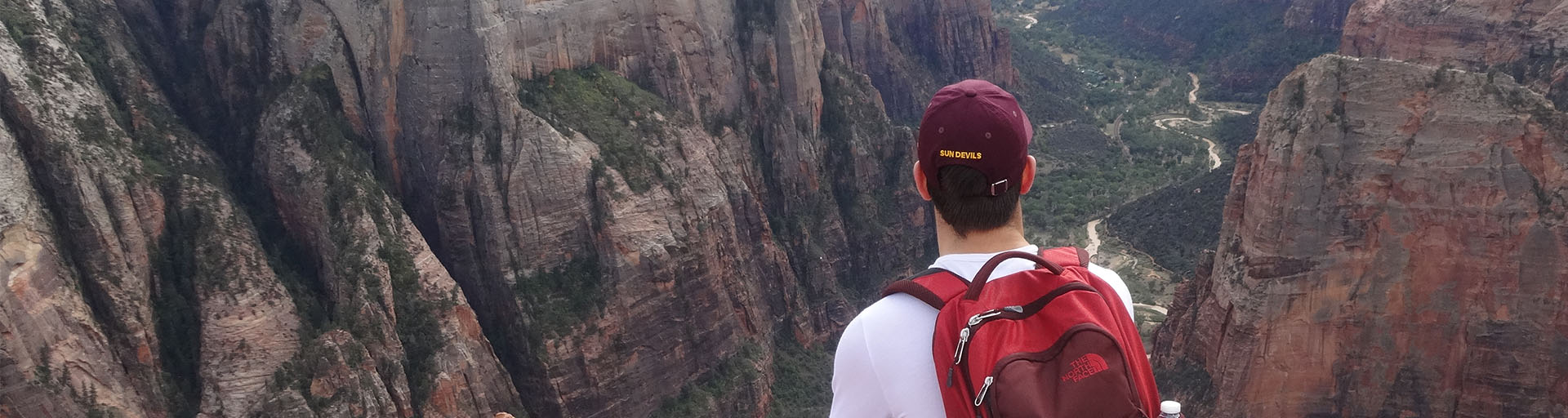 Student wearing a backpack and hat, overlooking an Arizona canyon