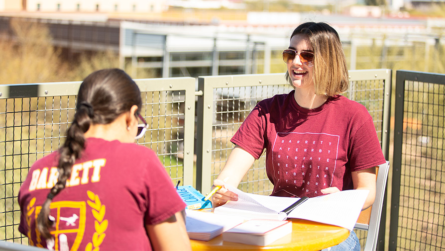 Two Barrett students on a balcony, talking while working on a project